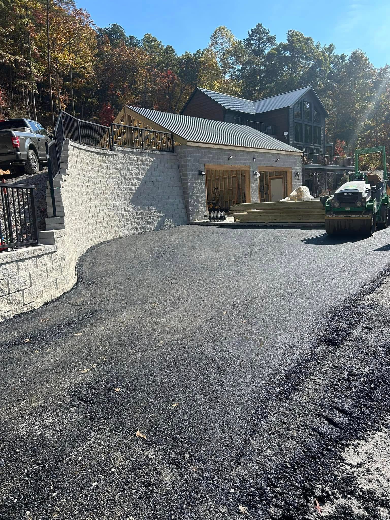 Gravel driveway leading to a stone building with a wooden roof; forest in background.