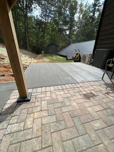 Brick patio leading to a gray surface, with a shed in the background. A wooden post is on the left.