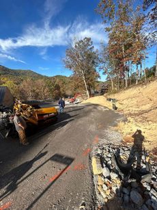 Construction site with a road being built, machinery, blue sky, trees.