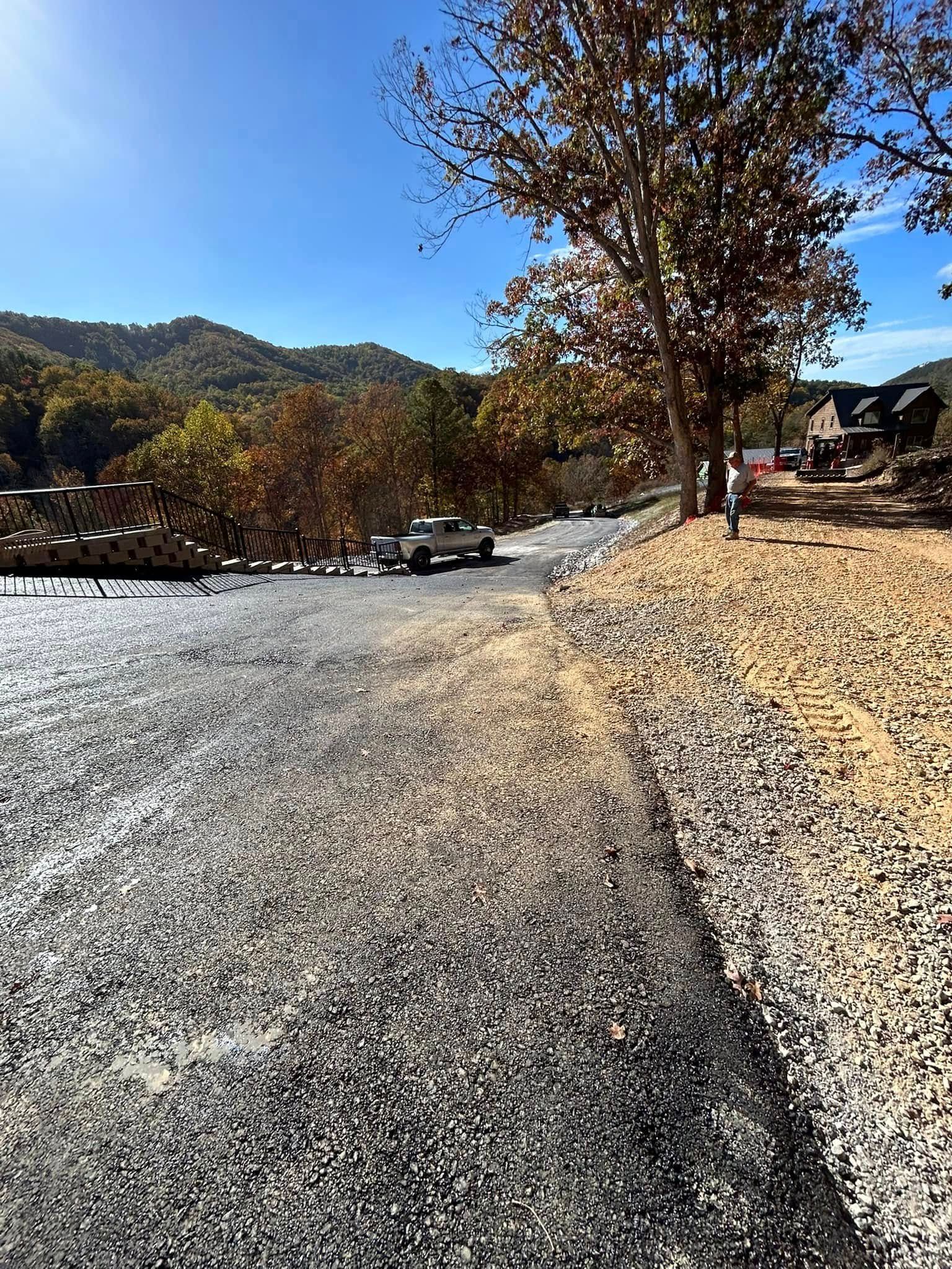 Gravel road with a white truck, trees, and hillside under a blue sky.