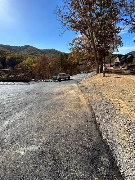 Gravel road with a white truck, trees, and hillside under a blue sky.