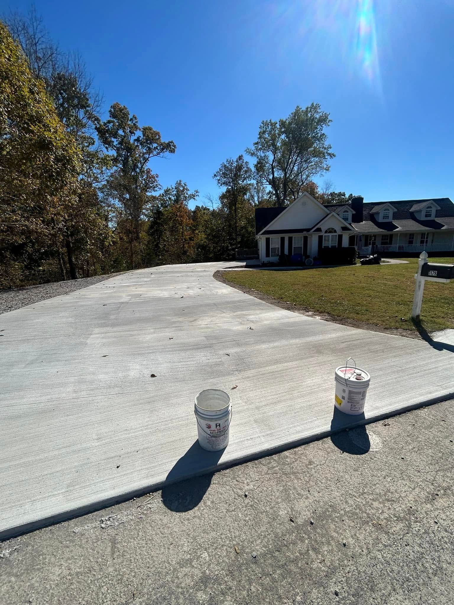 Concrete driveway leading to a house, bright blue sky, sunny day. Two buckets on driveway.