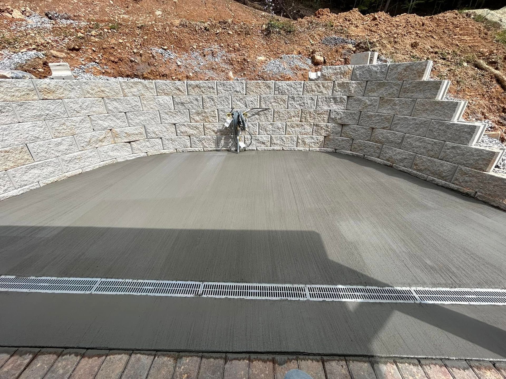 A freshly poured concrete patio with a retaining wall of stone and steps.
