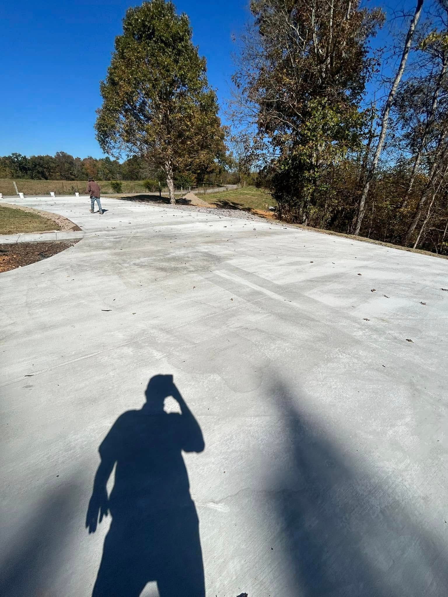 Shadow of person on concrete surface; two trees in background, blue sky.