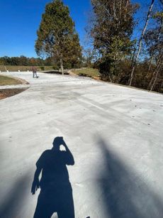 Shadow of person on concrete surface; two trees in background, blue sky.