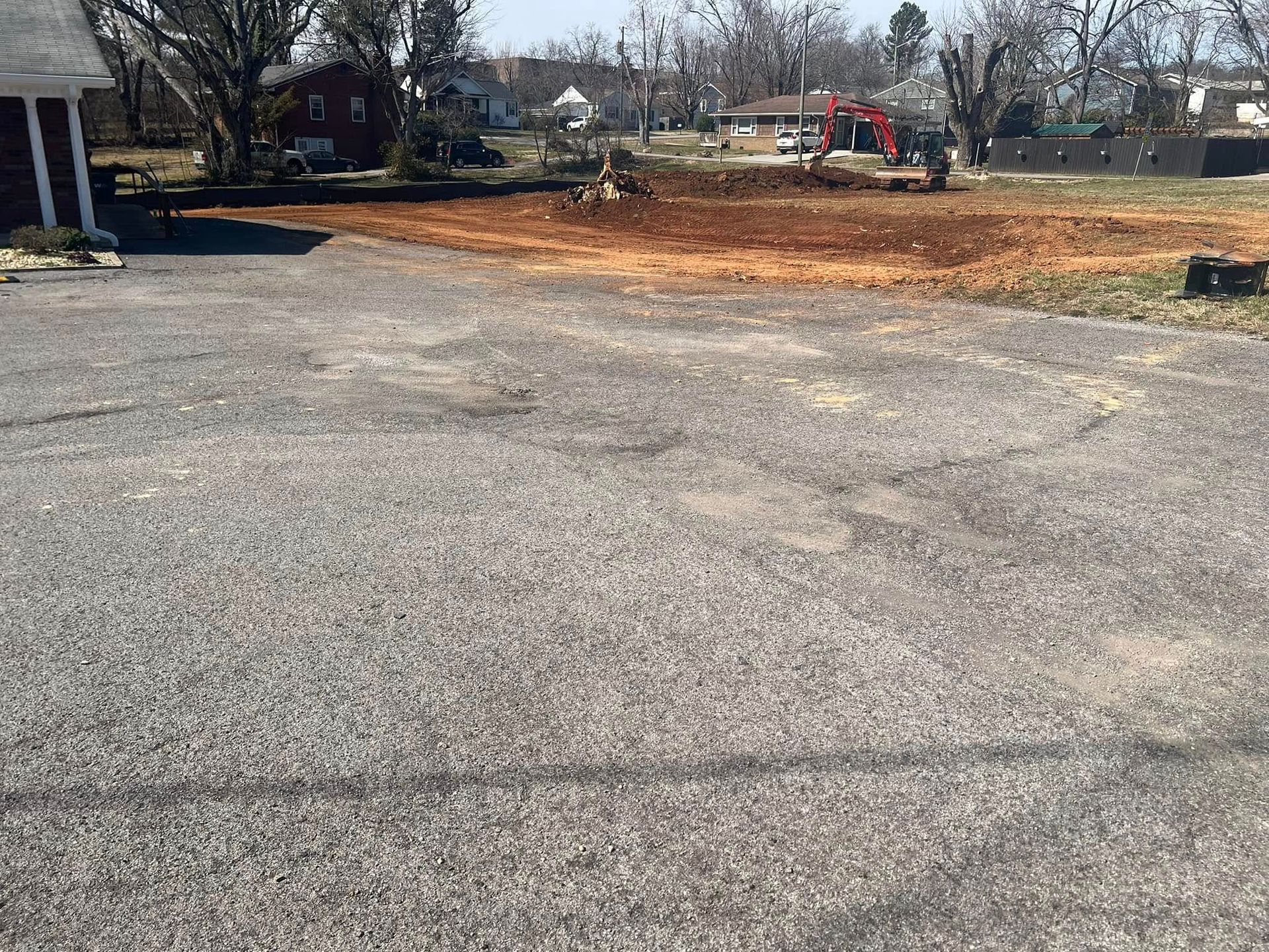 Gravel driveway with dirt construction site in the background, a small excavator and houses in view.