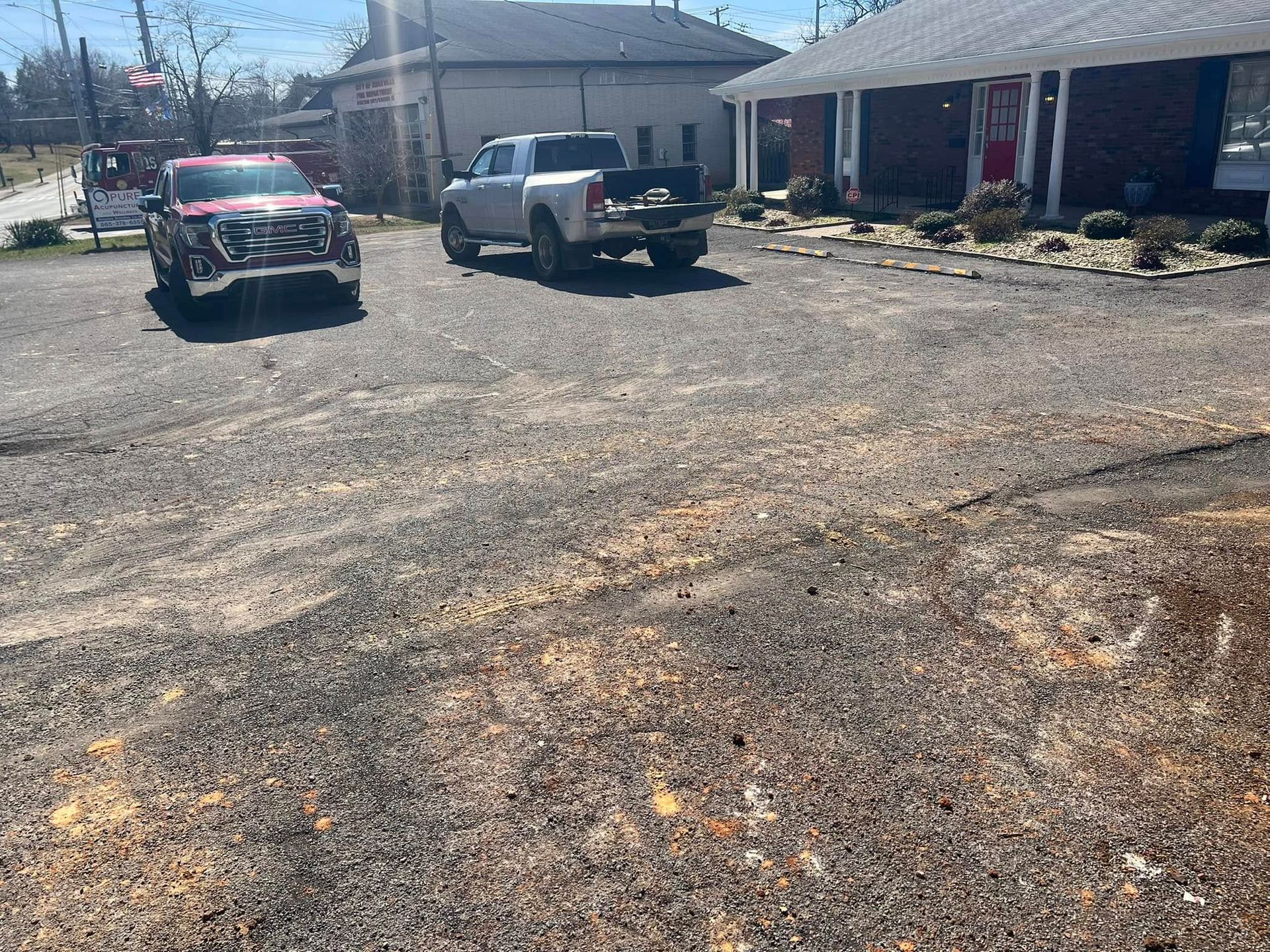 Two trucks on a gravel driveway, one red, one silver, in front of a building with a red door.