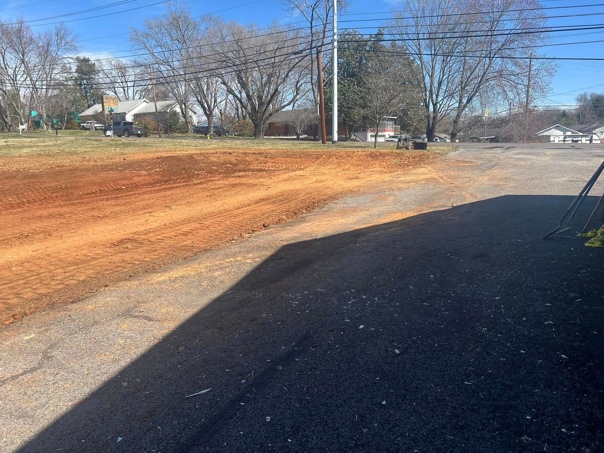 Gravel road transitions to dirt and grass, with power lines and houses in the distance.