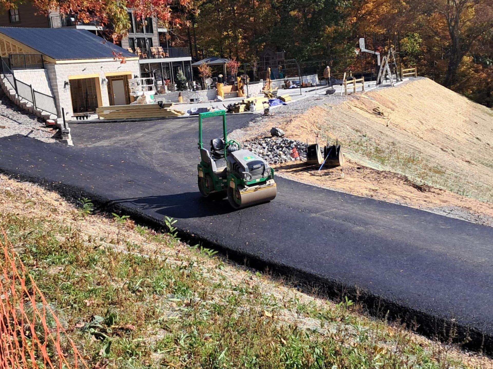 Asphalt paving in progress; a green roller compacts the new road surface near a building.