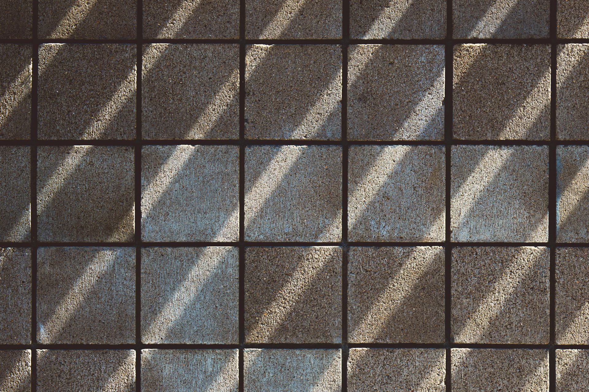 Shadows cast diagonally across a grid of square, textured tiles.