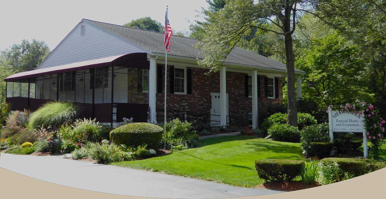 A brick building with white columns and an American flag. Landscaping and a sign are in front.