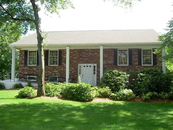 Brick house with white columns and door, black shutters, green bushes, and a green lawn.