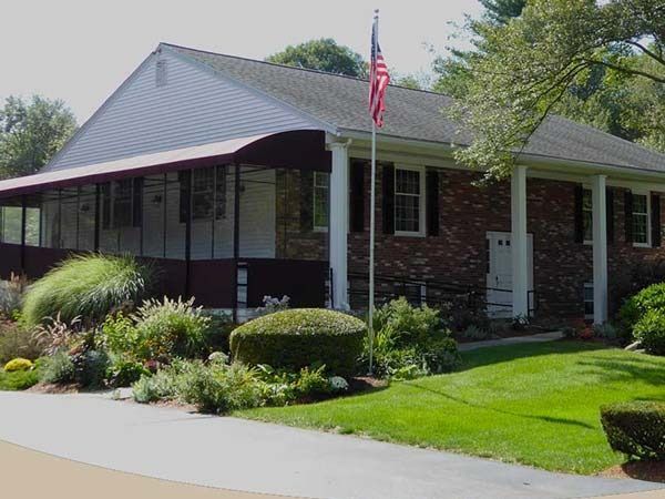 A one-story brick building with a covered porch and an American flag.