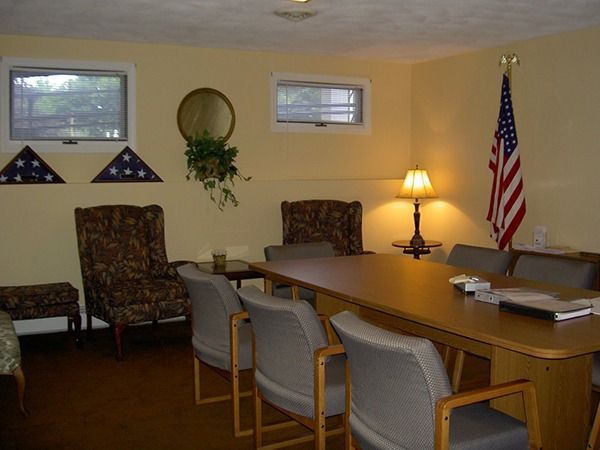 A room with a long table, chairs, an American flag, and memorial flags.