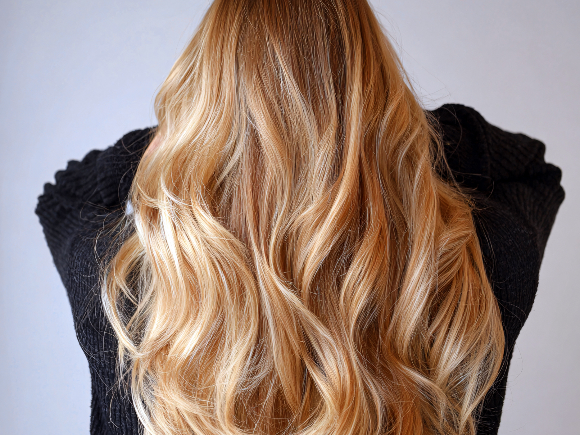 Long, wavy blonde hair cascading down a person's back; wearing a black sweater.