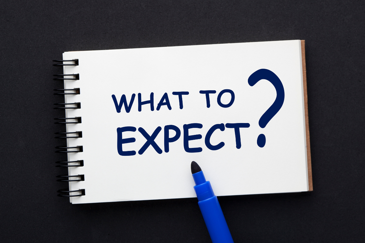 White notepad with “WHAT TO EXPECT?” written in blue, blue marker on black background.