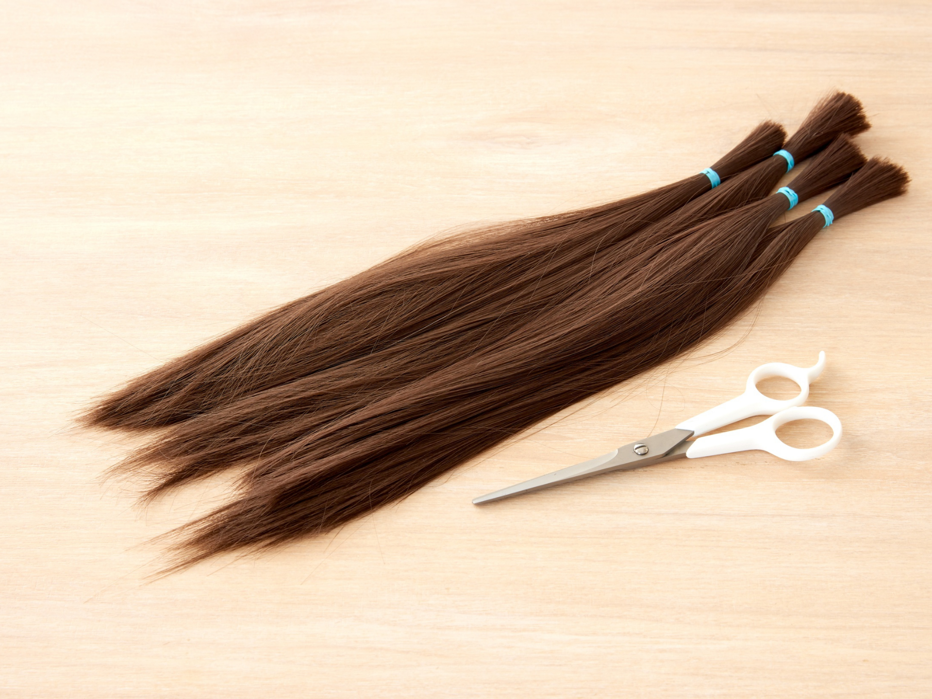 Brown hair extensions with blue bands, scissors on a light wood surface.