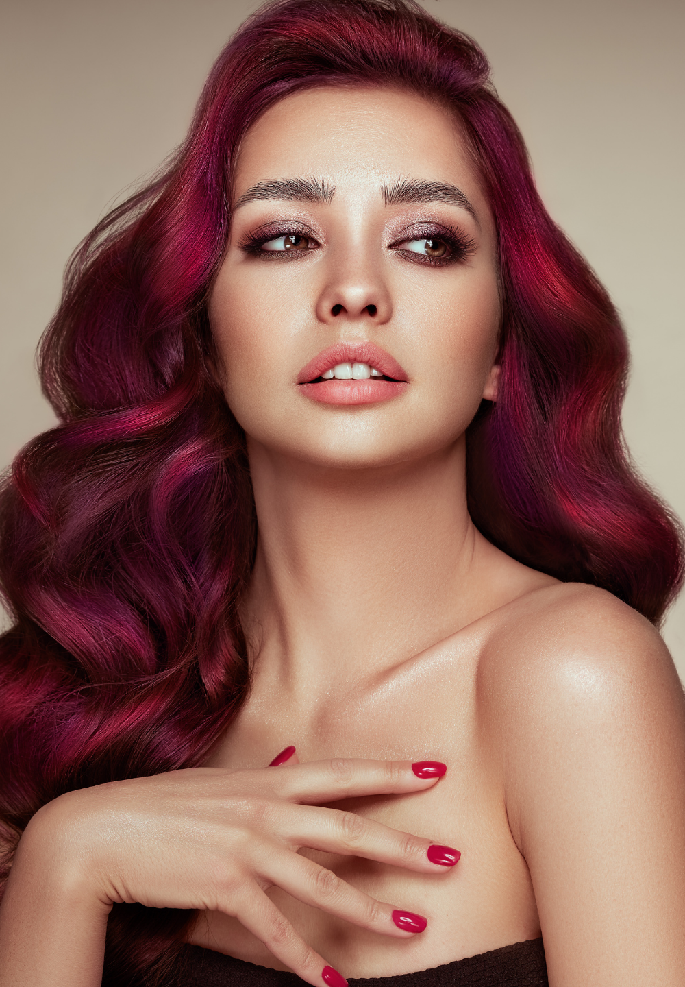 Woman with wavy, dark red hair, wearing a black top, with red nail polish, looking to the side.