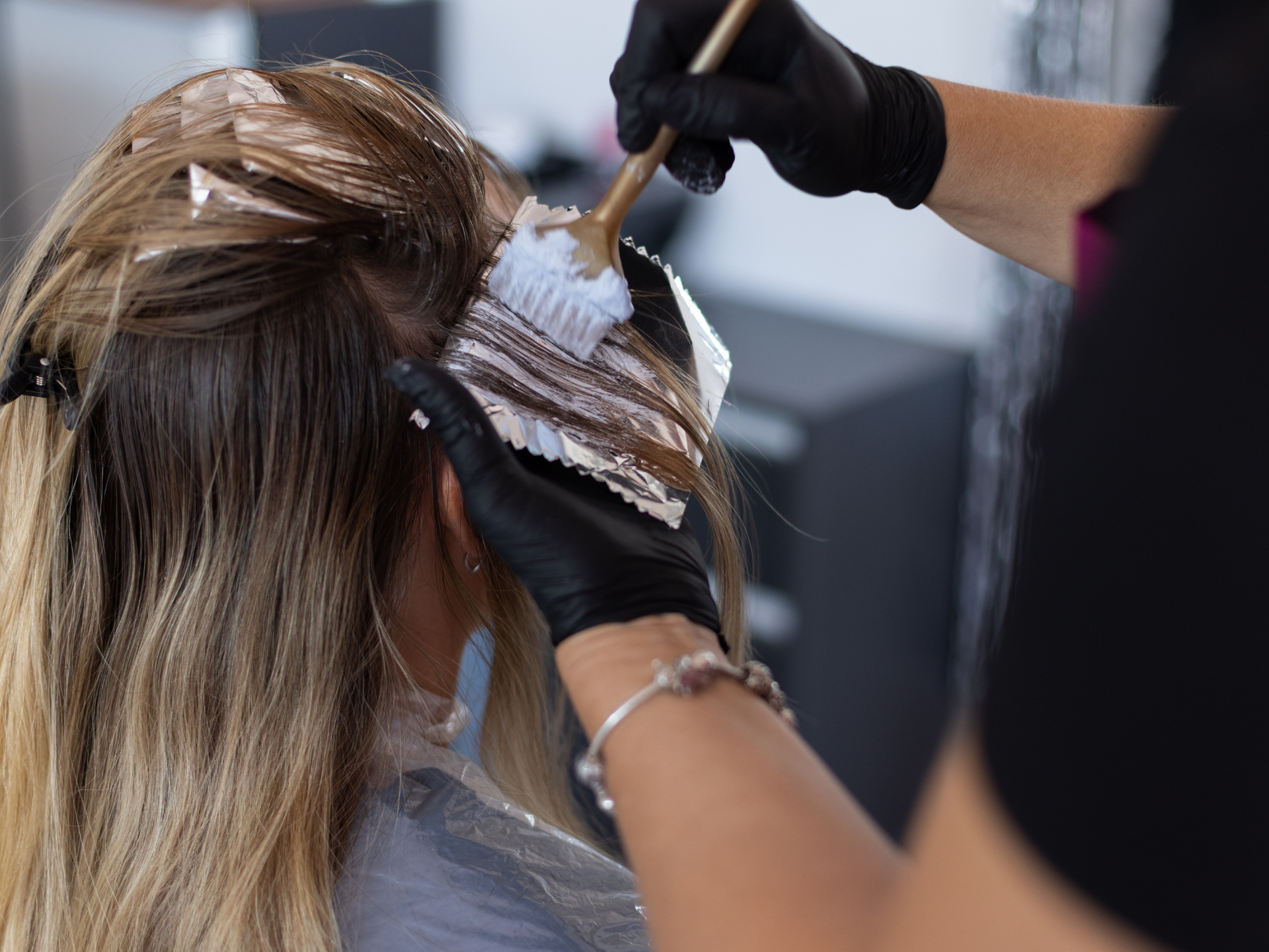 Hairdresser applying dye to blonde hair with a brush and foil in a salon.