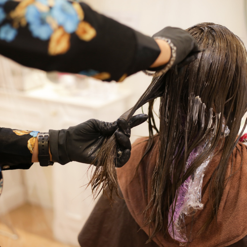 Hairdresser applying dye to a client's hair, in a salon, wearing black gloves.