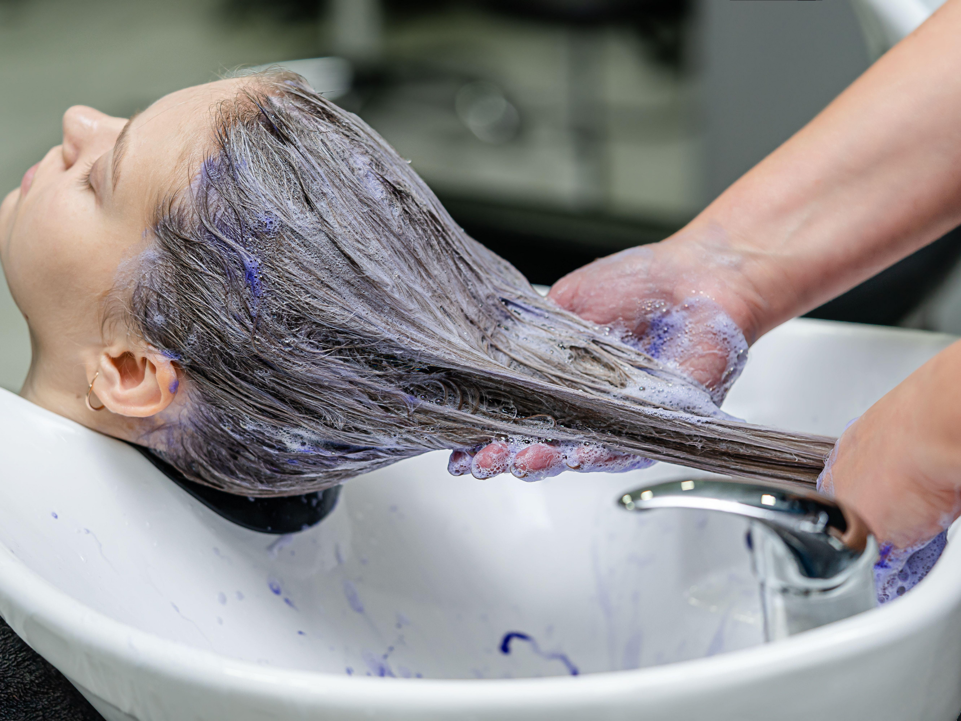 Person's hair being washed with purple shampoo in a salon sink.