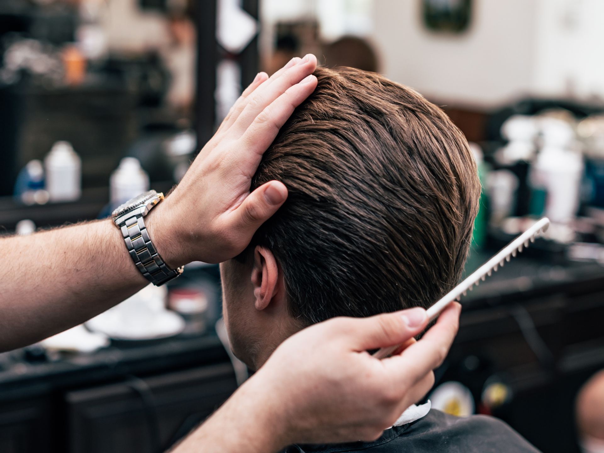 Barber combing and styling client's hair in a salon.