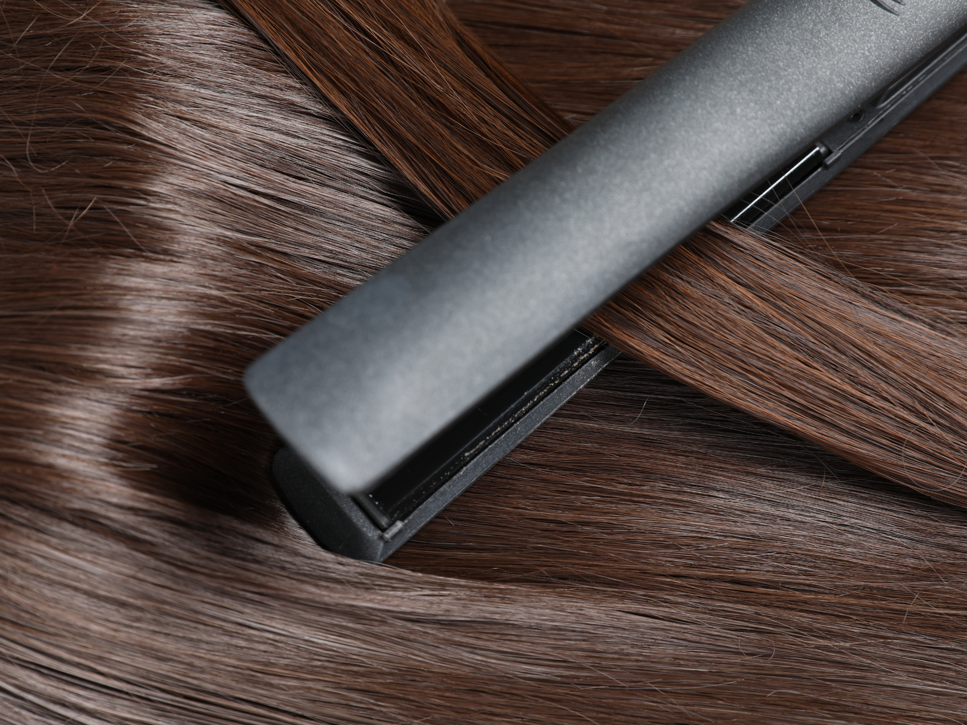 A flat iron smoothing a section of brown hair, resting on a bed of more hair.