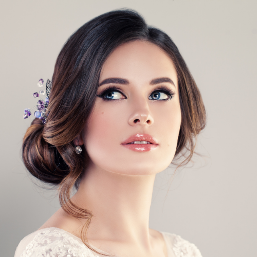 Woman with dark hair in updo, wearing makeup, looking upward, light background.