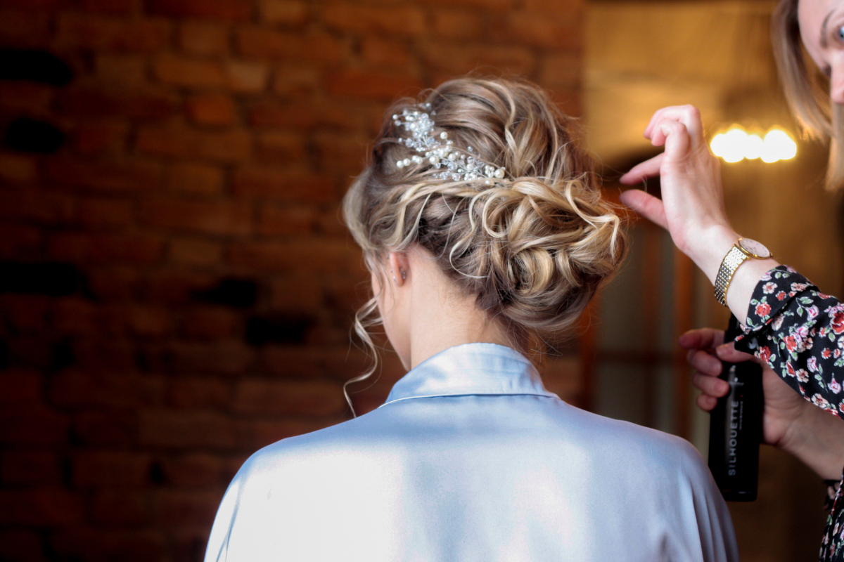 Woman's updo hairstyle being styled with hairspray; ornate hair accessory, soft lighting.