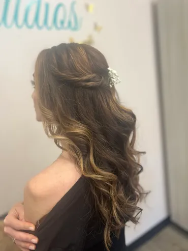 Woman with long, wavy brown hair, partially pinned up, wearing a black top. Hair styled with floral accent.