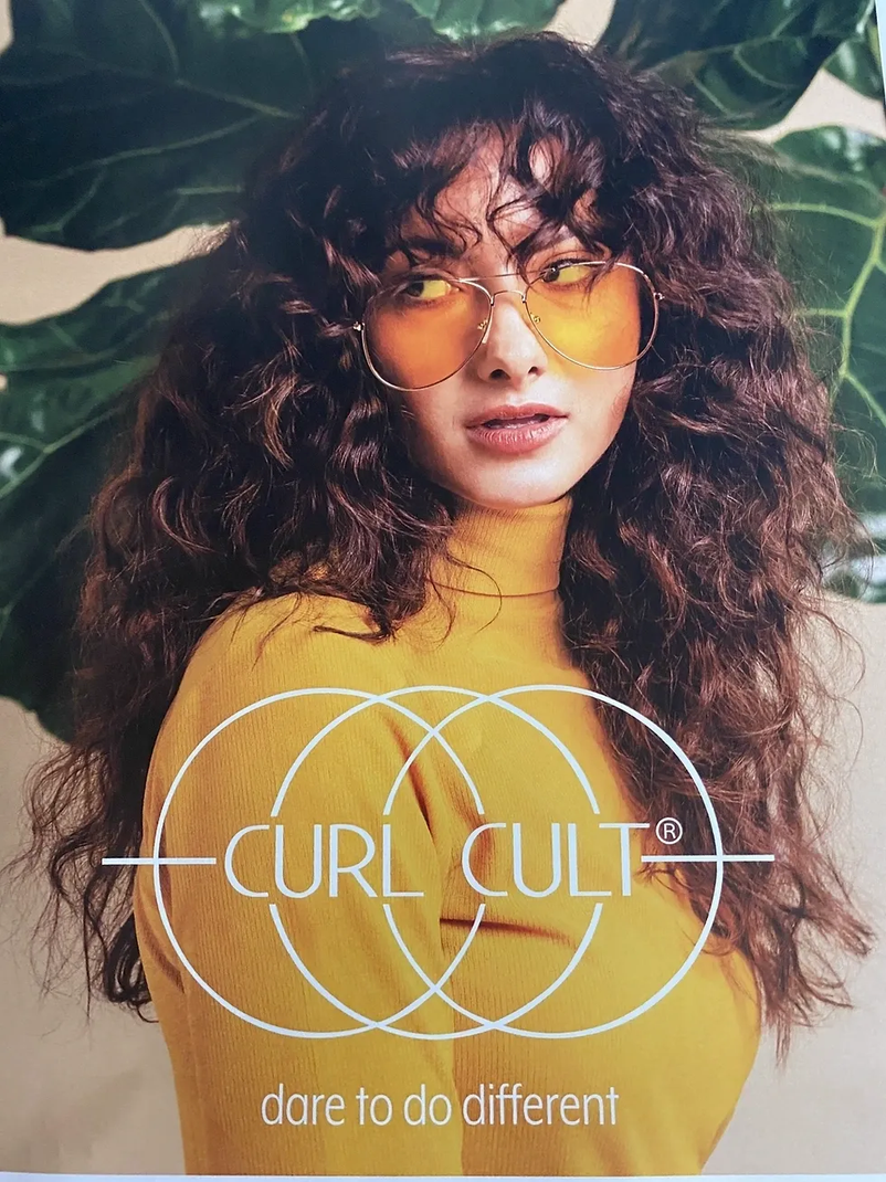 Woman with curly hair and yellow glasses, wearing yellow turtleneck,