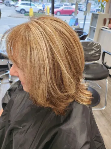 Woman with layered, highlighted, blonde-brown hair in a salon chair, looking to the side.