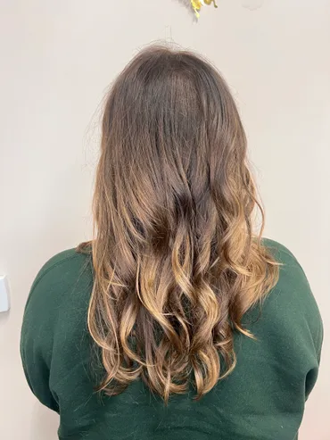 Woman from the back with brown hair styled with ombre effect and loose curls. She is wearing a dark green sweater.