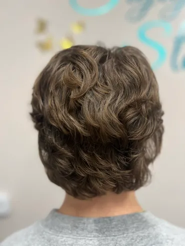 Back view of a person with a layered, wavy, brown hairstyle.