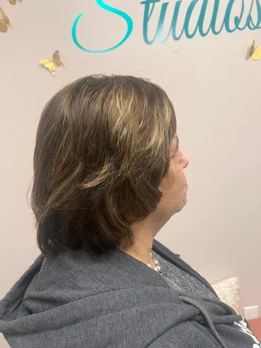 Woman with layered brown and blonde hair, gray sweatshirt, profile view in a salon.