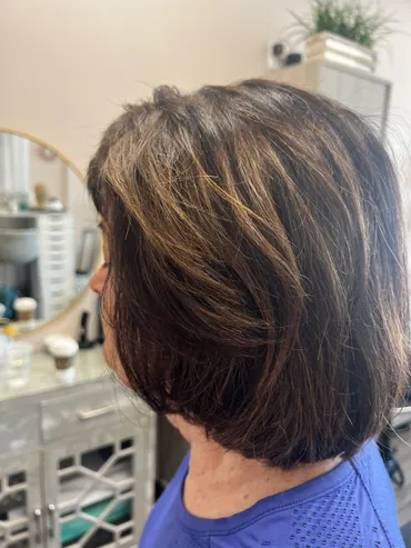 Woman with layered brown hair, some highlights, side view in a salon setting.