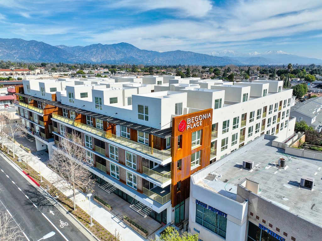 Modern, white apartment building with rusty-orange accents and balconies, mountains in the background.