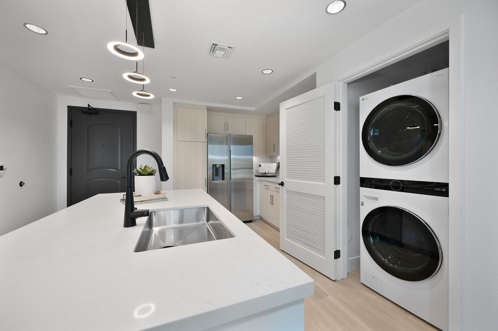 Modern kitchen with white countertops, island, stainless steel appliances, and stacked washer/dryer in a closet.