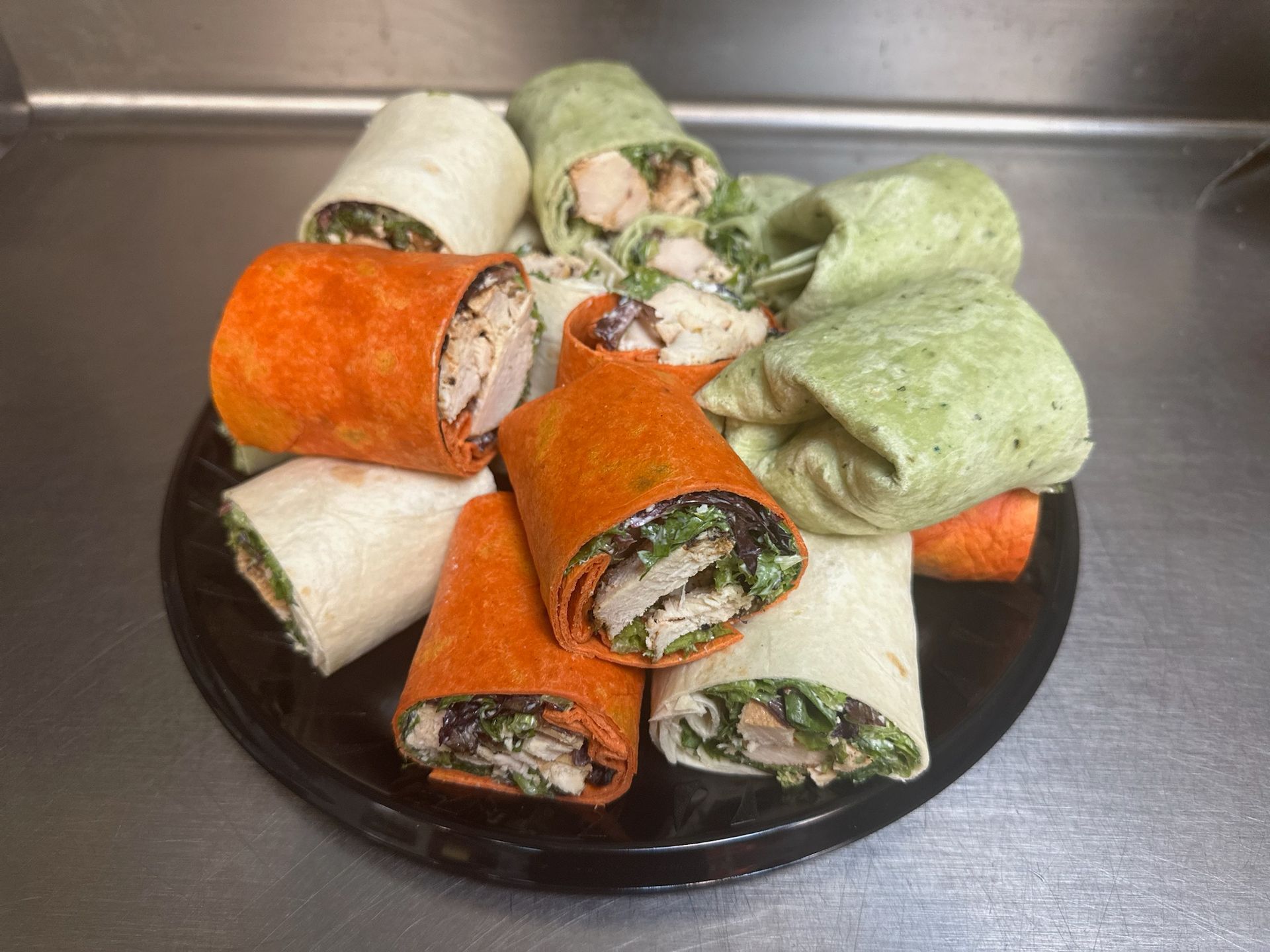 a black plate topped with a variety of wraps on a table .