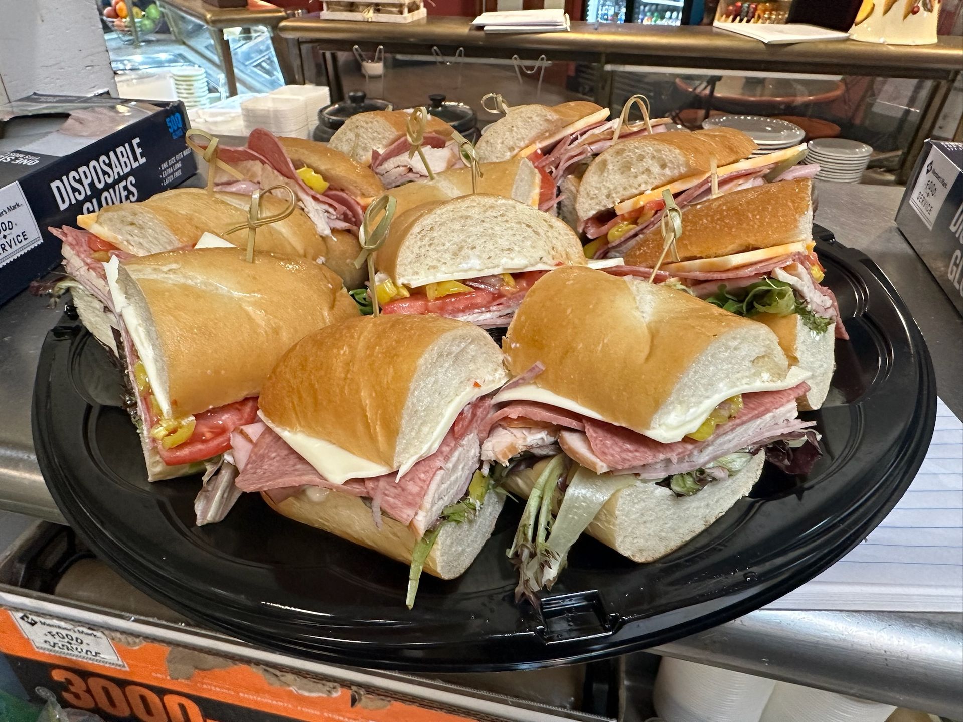 a tray of sub sandwiches on a table with a box of disposable gloves in the background .