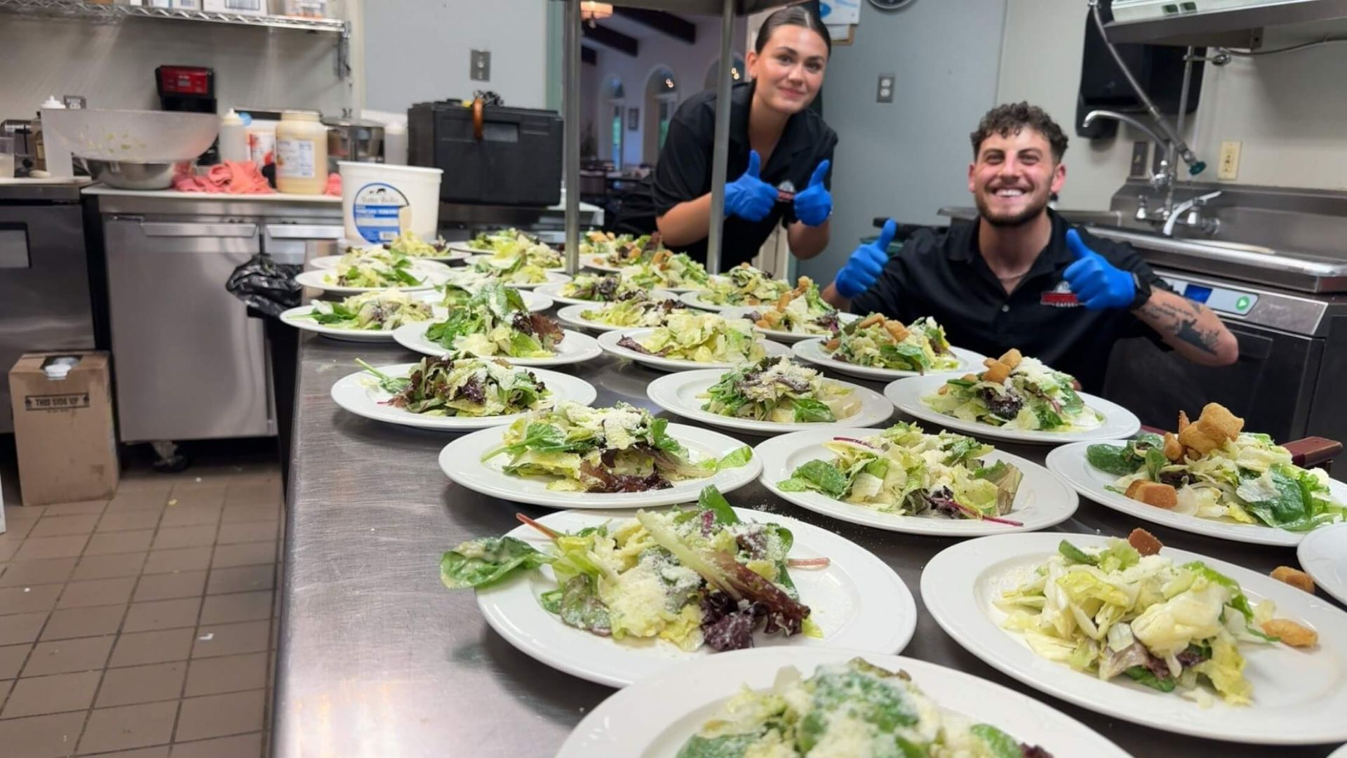 A man and a woman are standing in a kitchen surrounded by plates of food.