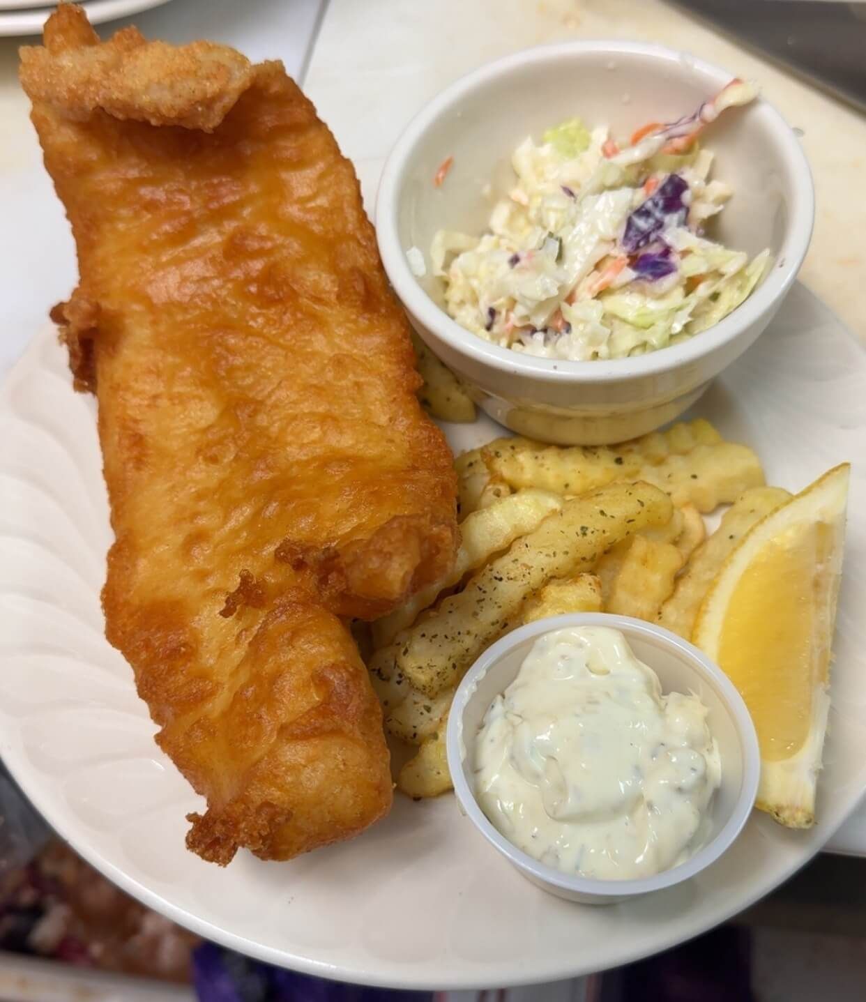 A plate of fish and chips with coleslaw and tartar sauce.