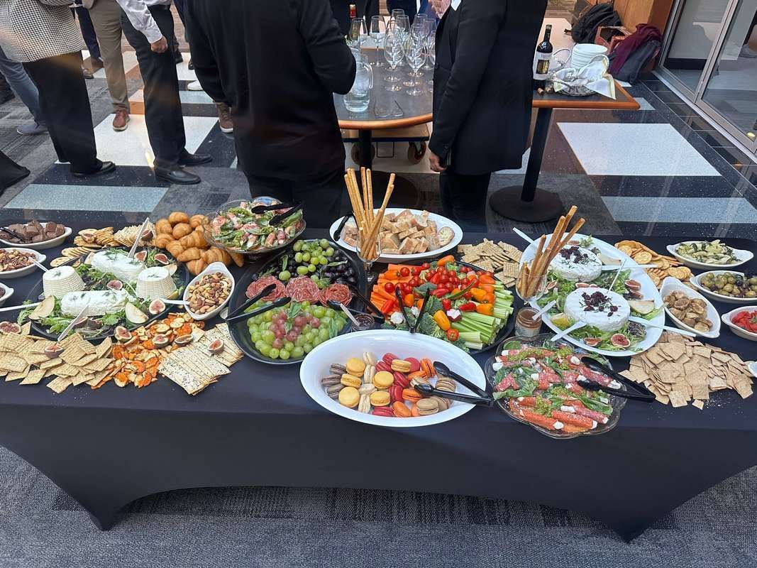 A table topped with plates of food and people standing around it.