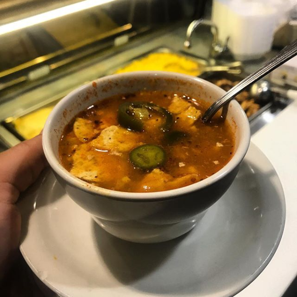 a person is holding a bowl of soup with a spoon in it