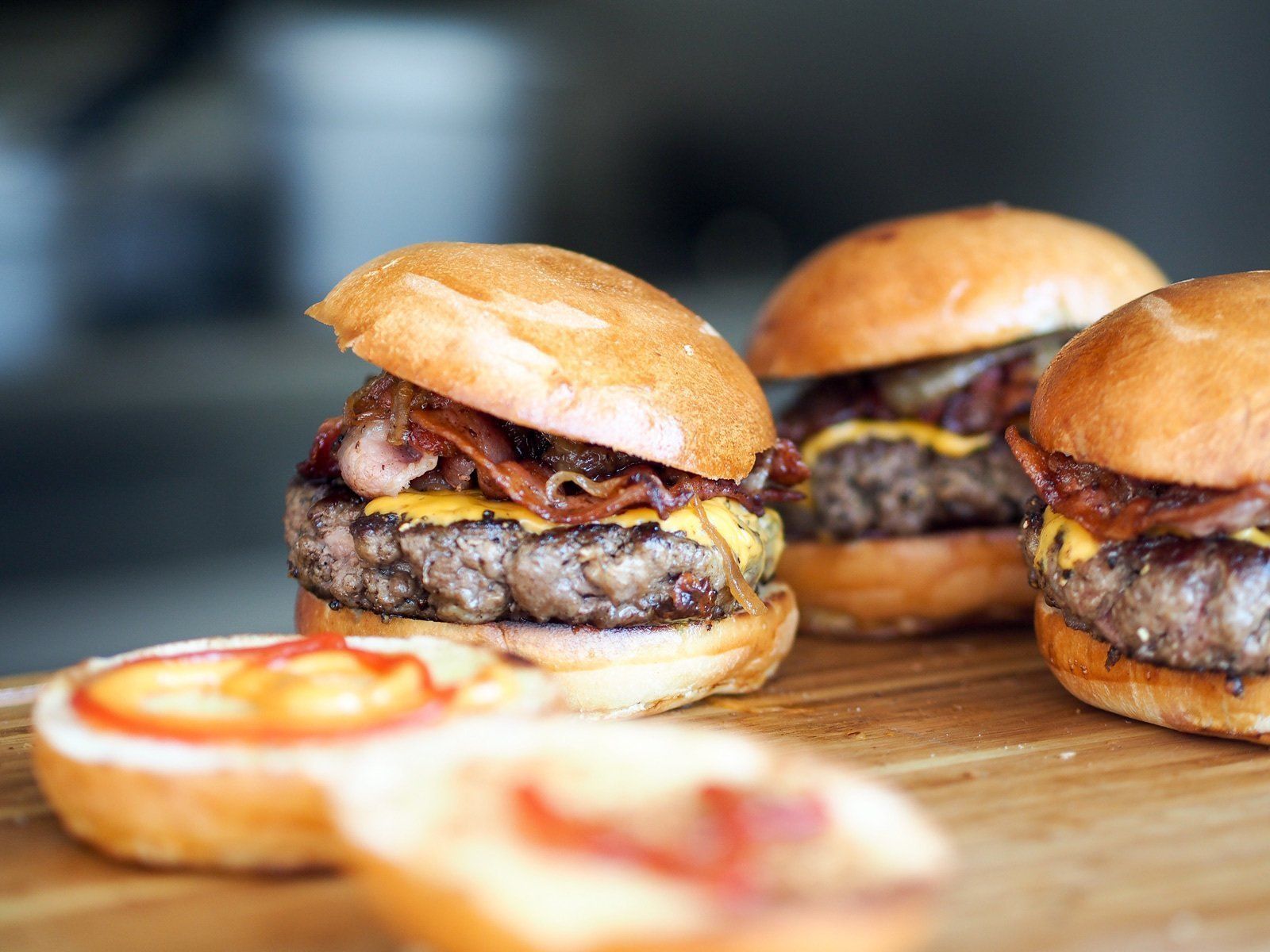 three hamburgers are sitting on a wooden cutting board .