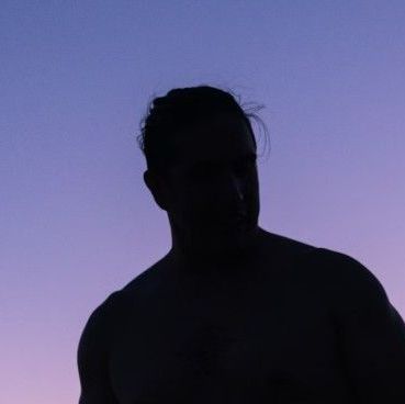 A silhouette of a man without a shirt against a purple sky.