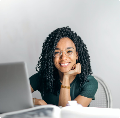 A woman is smiling while sitting in front of a laptop computer.