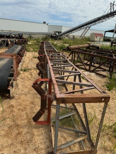 A large metal structure is sitting in the dirt near a conveyor belt
