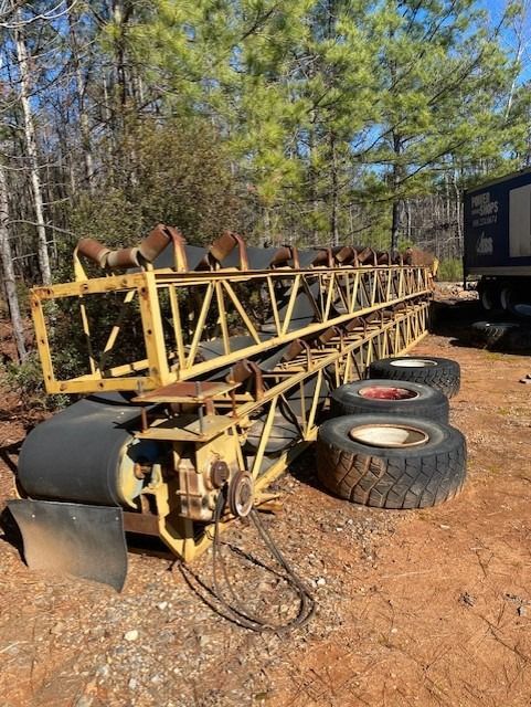 A conveyor belt is sitting in the dirt next to a truck.