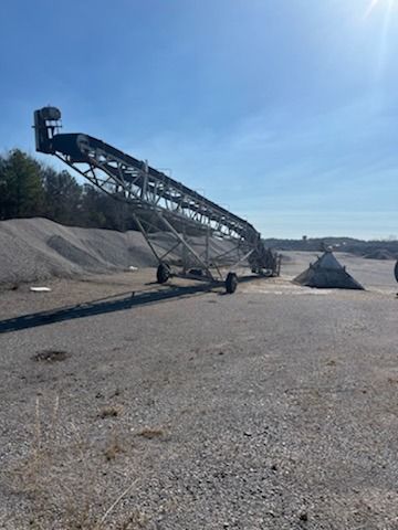 A conveyor belt is sitting in the middle of a gravel field.